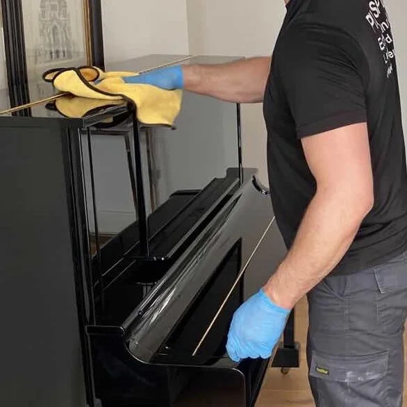 An upright piano being cleaned and prepared by a PianoSpeed crew member